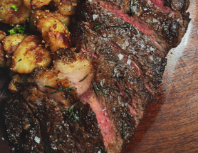 A close up of a steak and potatoes on a wooden plate.