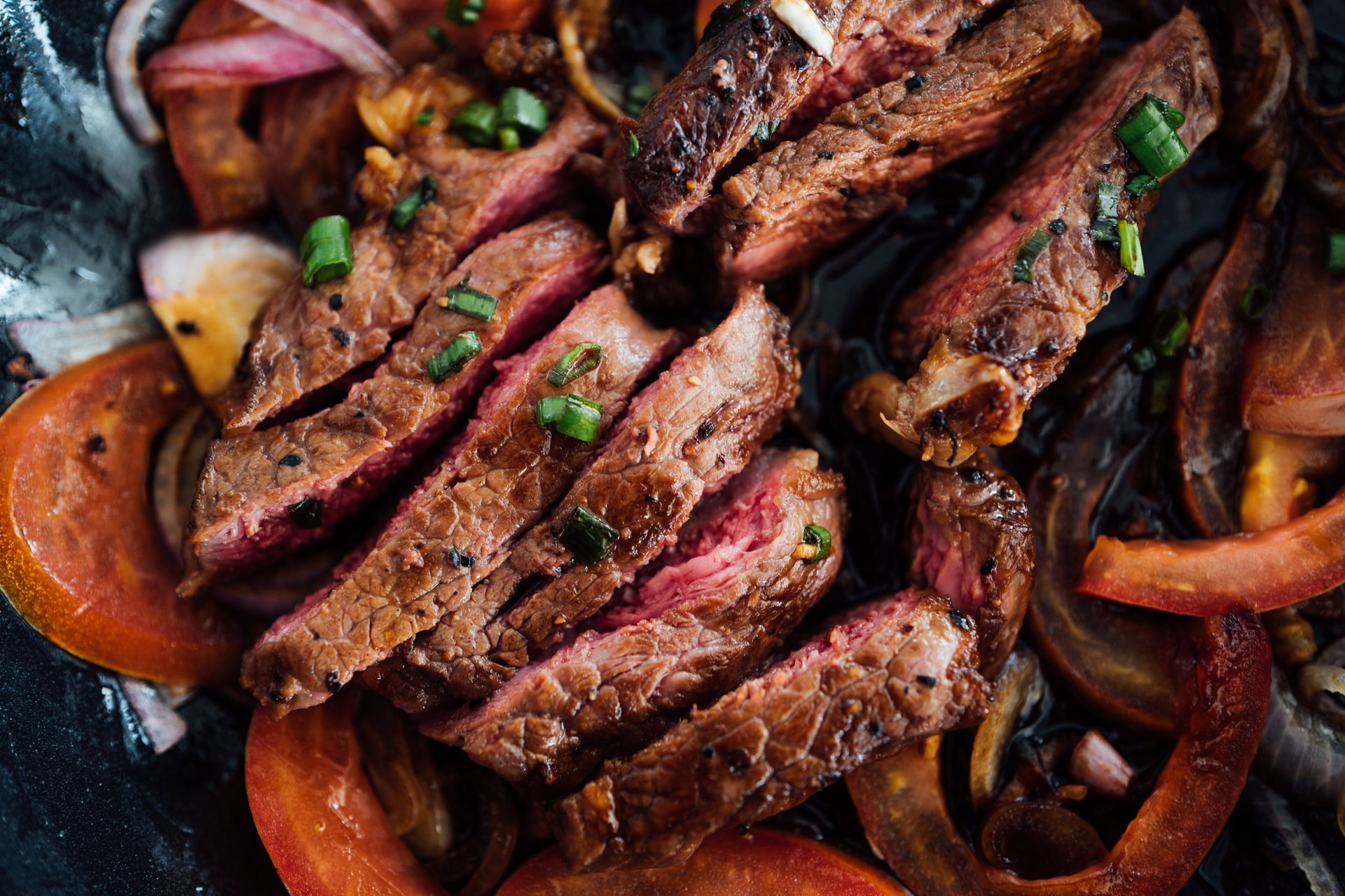 A close up of a steak with tomatoes and onions on a plate.