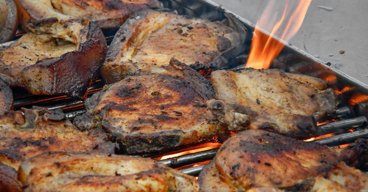 A close up of meat cooking on a grill with flames coming out of it.