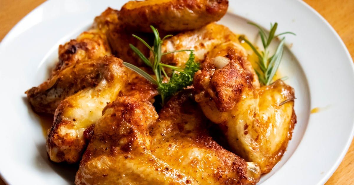 A white plate topped with chicken wings and rosemary on a wooden table.