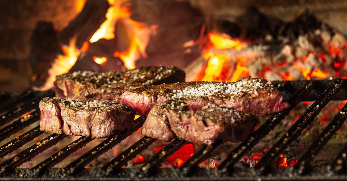 Two steaks are cooking on a grill over a fire.