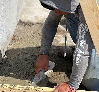 A man is kneeling down and using a trowel to spread cement on a sidewalk
