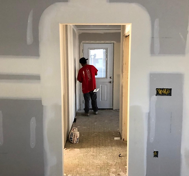 A man in a red shirt is standing in a hallway next to a door