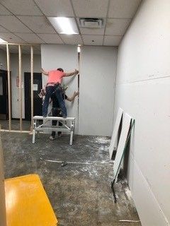 Two men are working on a wall in a room