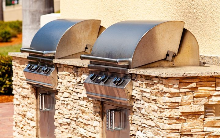 two full-size outdoor stainless gas grills built into a granite countertop area with cut natural stone surround
