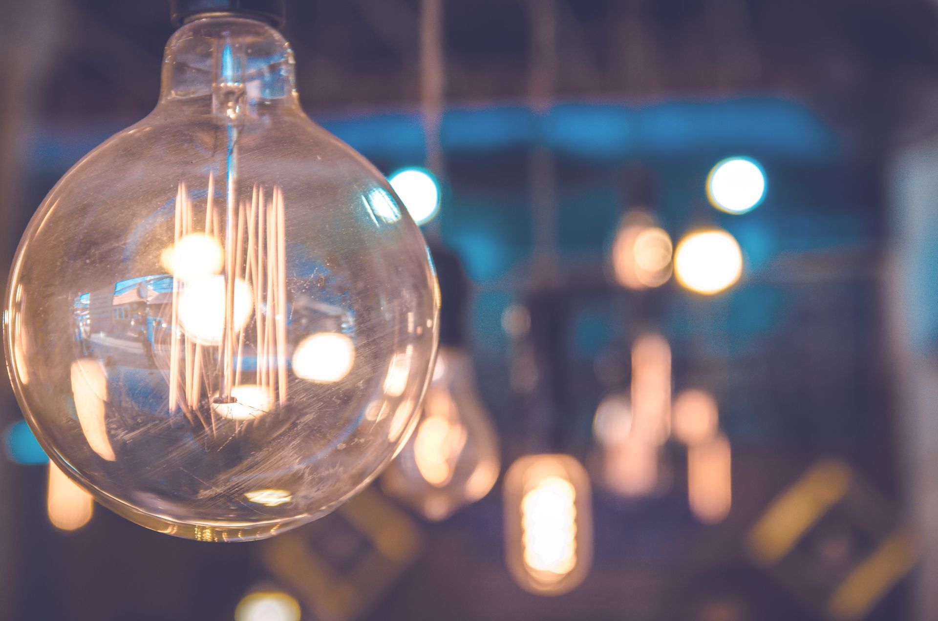 Primo piano di una lampadina rotonda e luminosa con filamenti visibili, altre lampadine sfocate sullo sfondo.