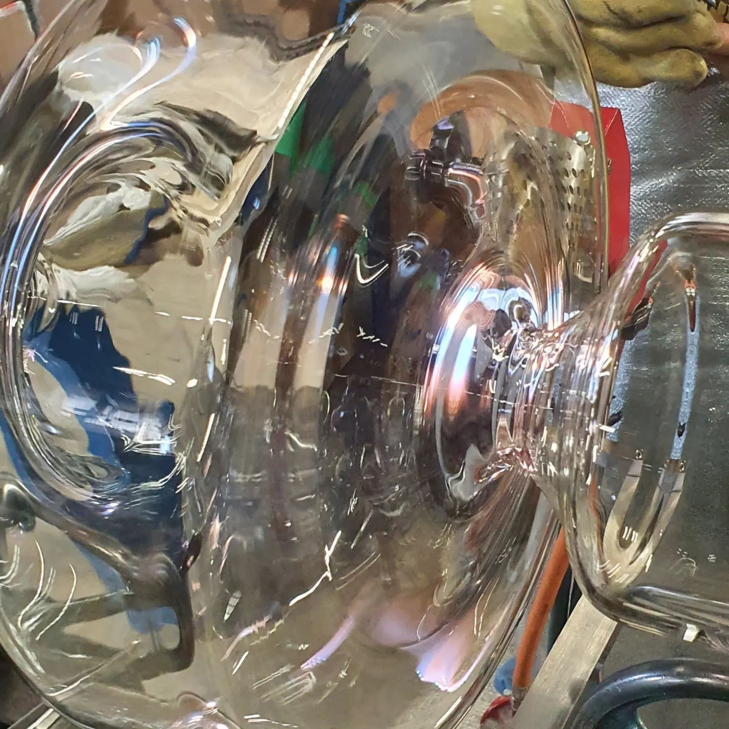 Una brocca di vetro trasparente con manico riflette gli oggetti circostanti, posta su una superficie riflettente.