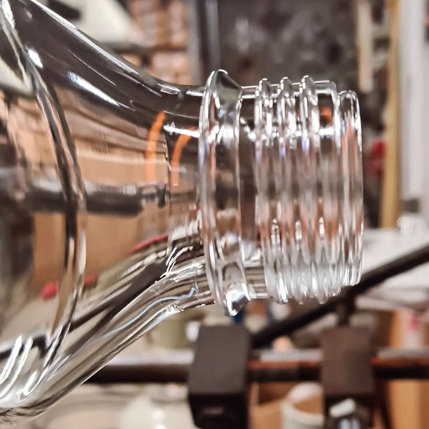 Primo piano del collo di una bottiglia di vetro trasparente con bordo filettato. Sfondo sfocato di un laboratorio.