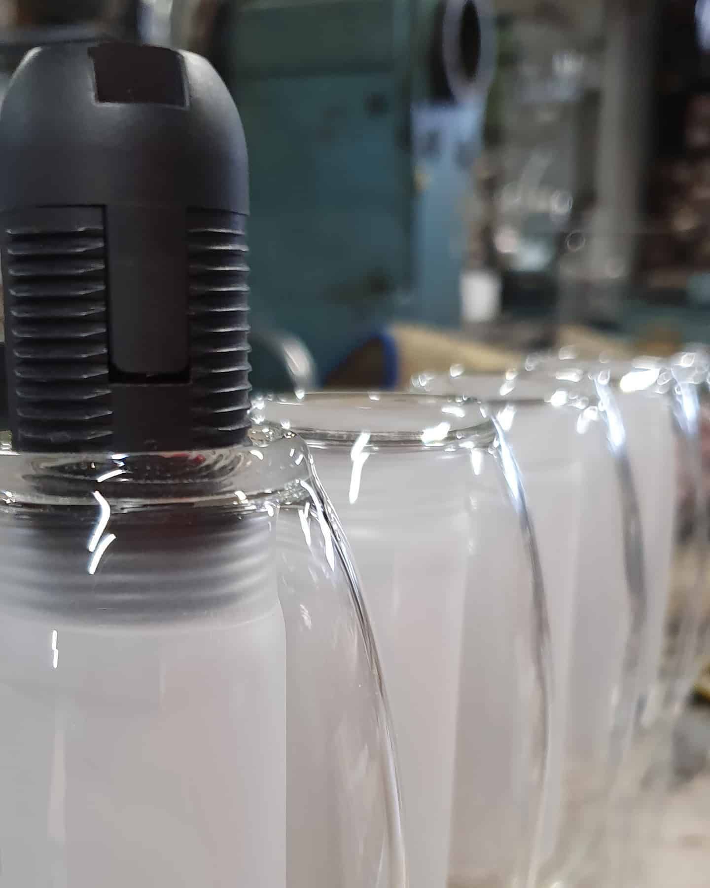 Lampadina con tappo nero in una fila di barattoli di vetro pieni di liquido bianco, in un ambiente di laboratorio.