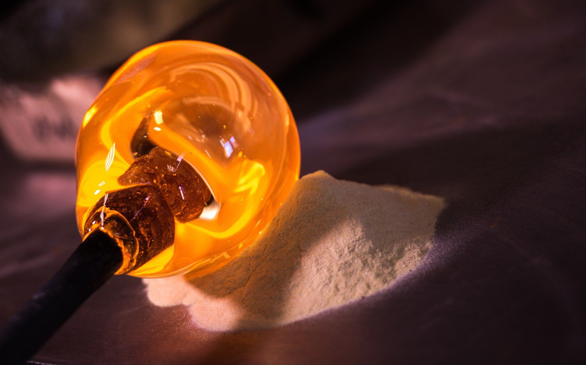 Bolla di vetro arancione fuso su un tubo nero, appoggiata vicino a un mucchio di polvere bianca.