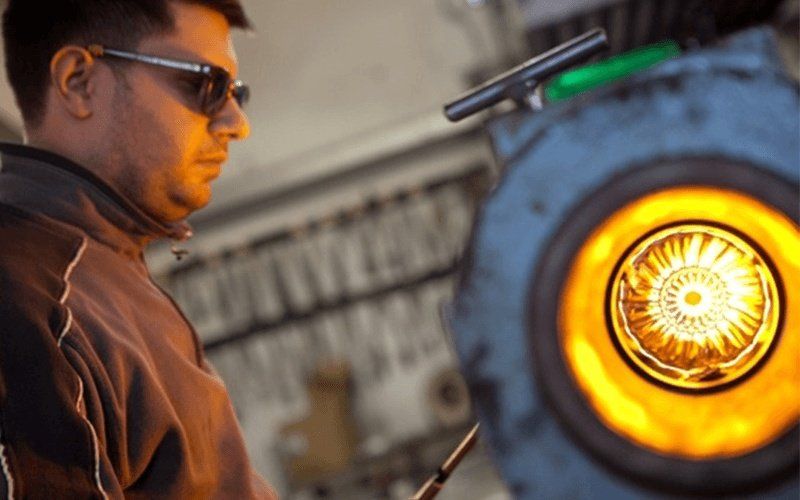 Uomo con occhiali da sole che lavora con il vetro fuso in una fornace.