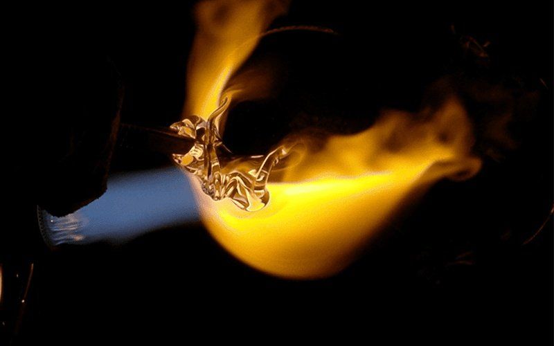 Vetro modellato da una fiamma gialla su sfondo nero.