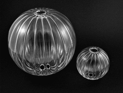 Due oggetti trasparenti, sferici e scanalati, con aperture, probabilmente contenitori, su uno sfondo scuro.