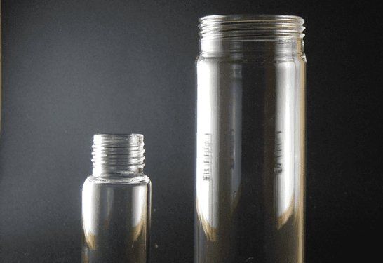 Due bottiglie di vetro trasparente, una bassa e una alta, su uno sfondo scuro.