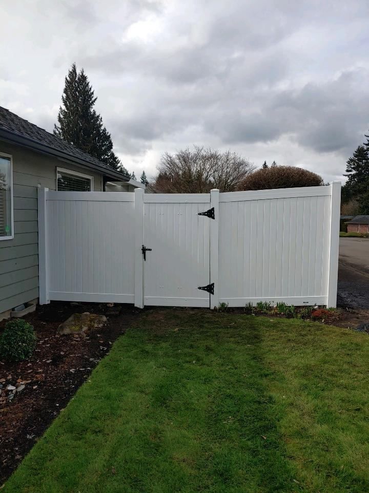 White vinyl gate and fence beside a house, with a green lawn and cloudy sky.