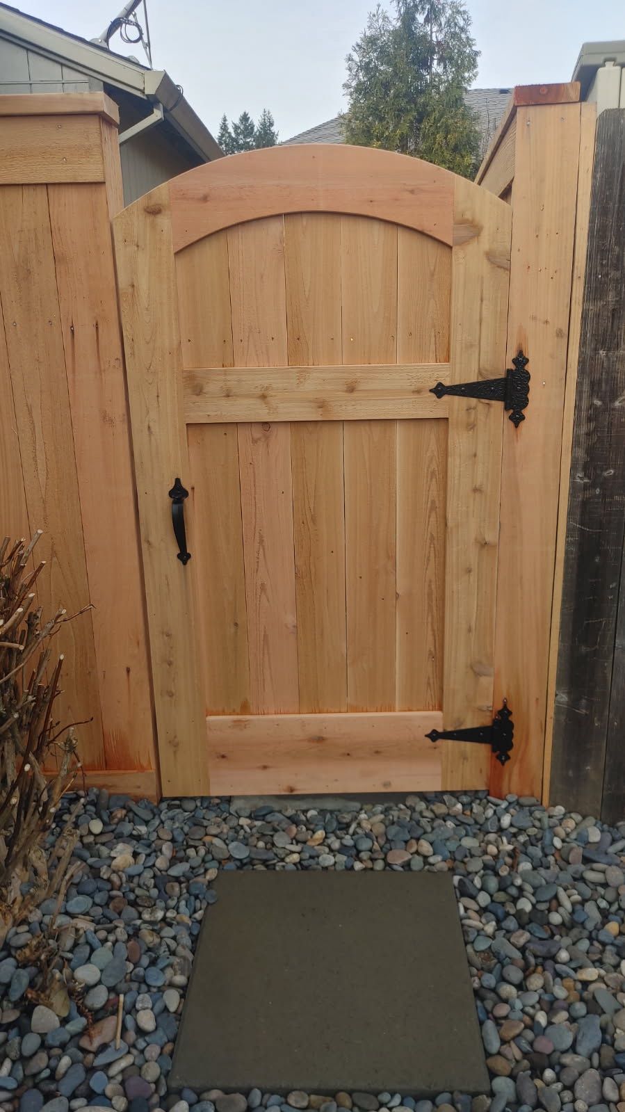 Wooden garden gate with black latch, gravel path, and a small mat in front