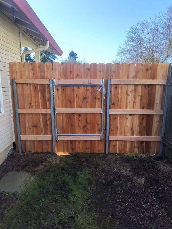 Backyard wooden fence with a metal gate section and patchy grass in front
