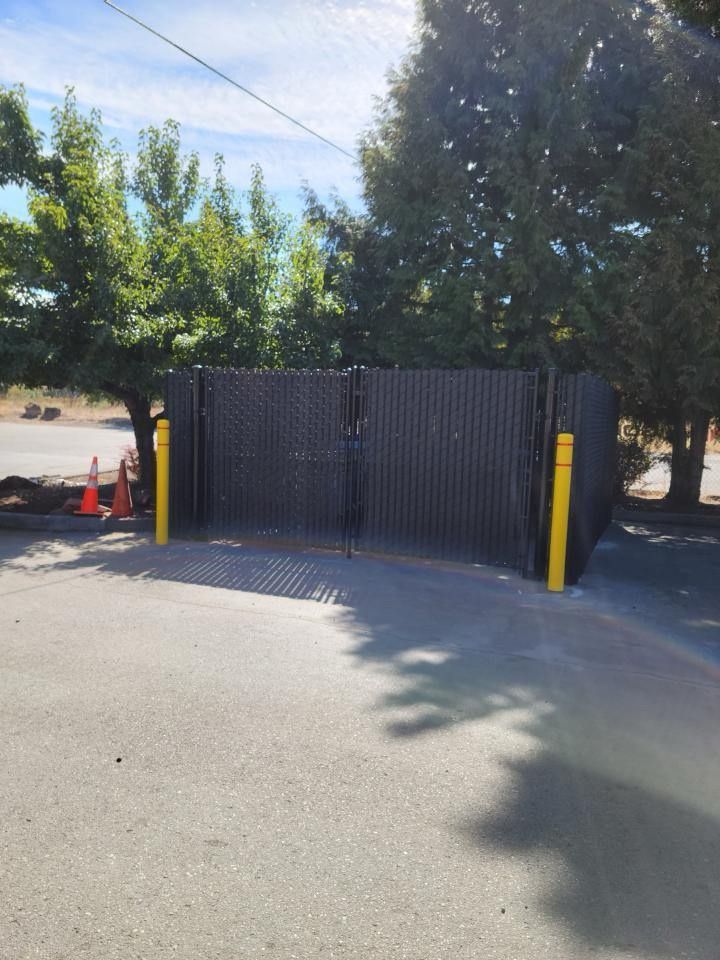 Black fence and yellow posts blocking a driveway, with orange cones and trees in the background.