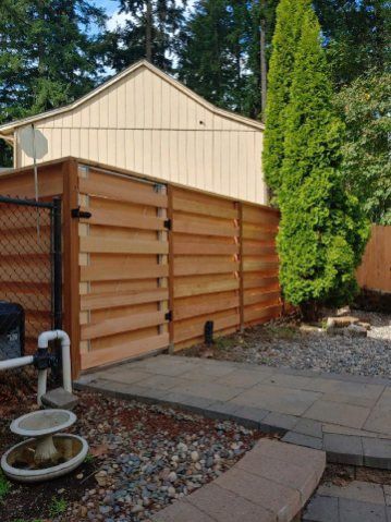 Backyard with tan shed, wooden privacy fence, paved path, gravel, and tall evergreen hedge