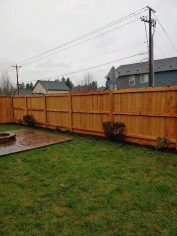 Backyard with green lawn, wooden fence, concrete patio, and cloudy sky with utility poles.
