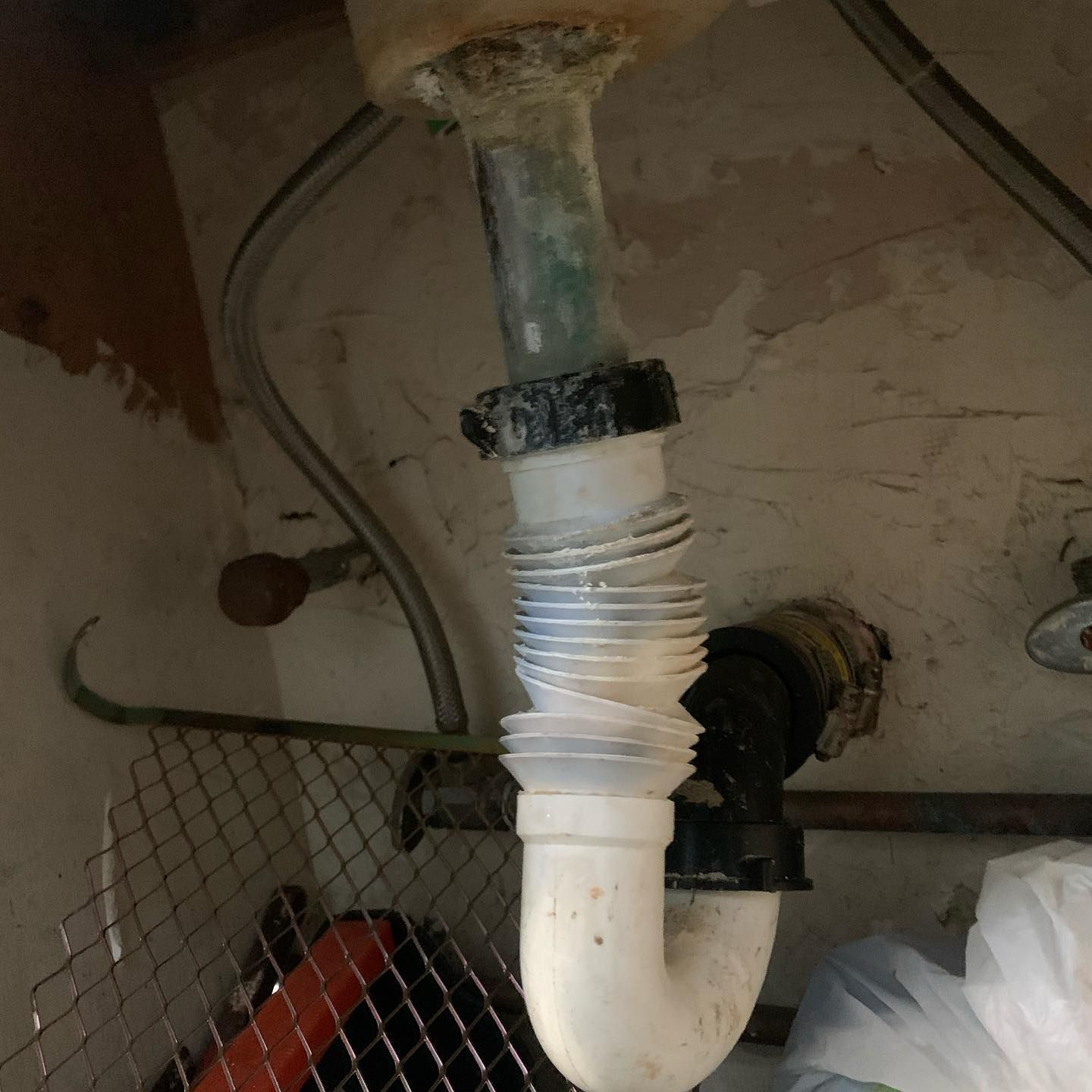 White, plastic, accordion-style drainpipe under a sink, with signs of wear and discoloration. 