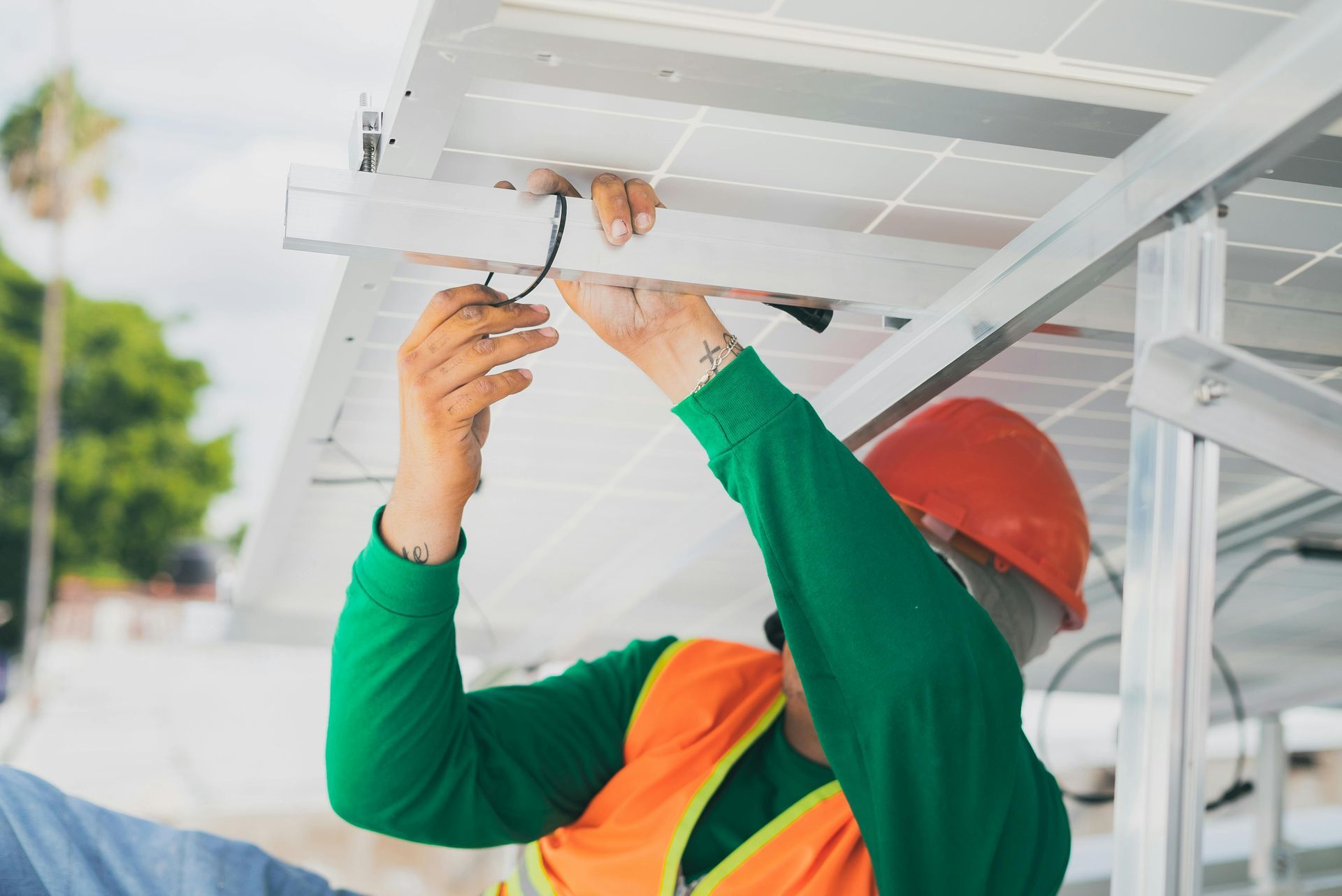 Person in hard hat installs solar panels on a metal frame outdoors.