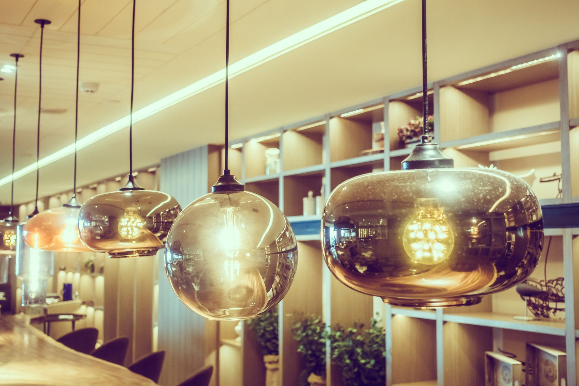 Shiny, globe-shaped pendant lights hang above a bar, with shelves and plants in the background.