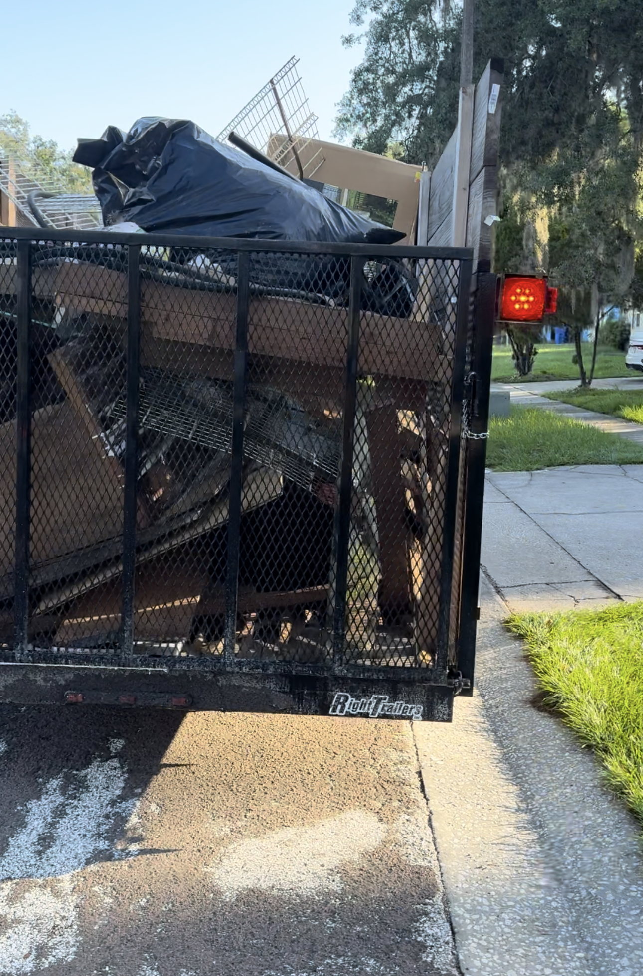 A trailer filled with junk is parked on the side of the road.