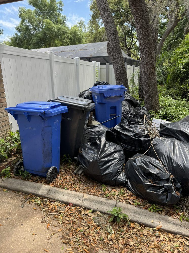 A pile of trash bags and trash cans on the side of the road.