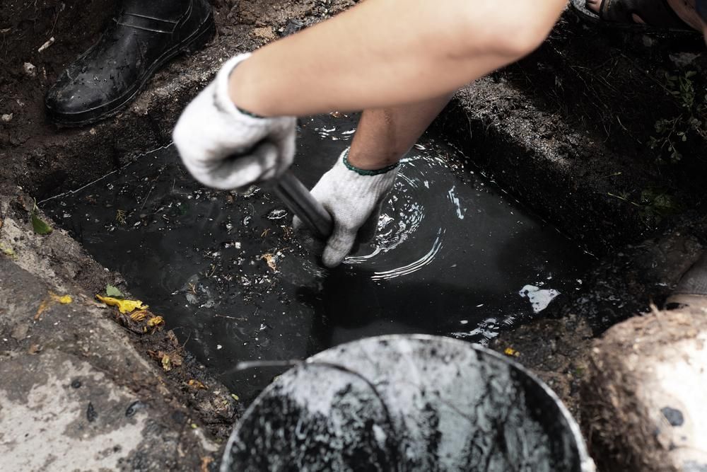 A Person is Cleaning a Hole in the Ground With a Bucket of Water — Wahoo Plumbing in Maroochydore, QLD