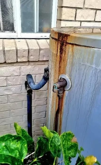 A Rusty Water Tank is Sitting Next to a Brick Wall — Wahoo Plumbing in Buderim, QLD
