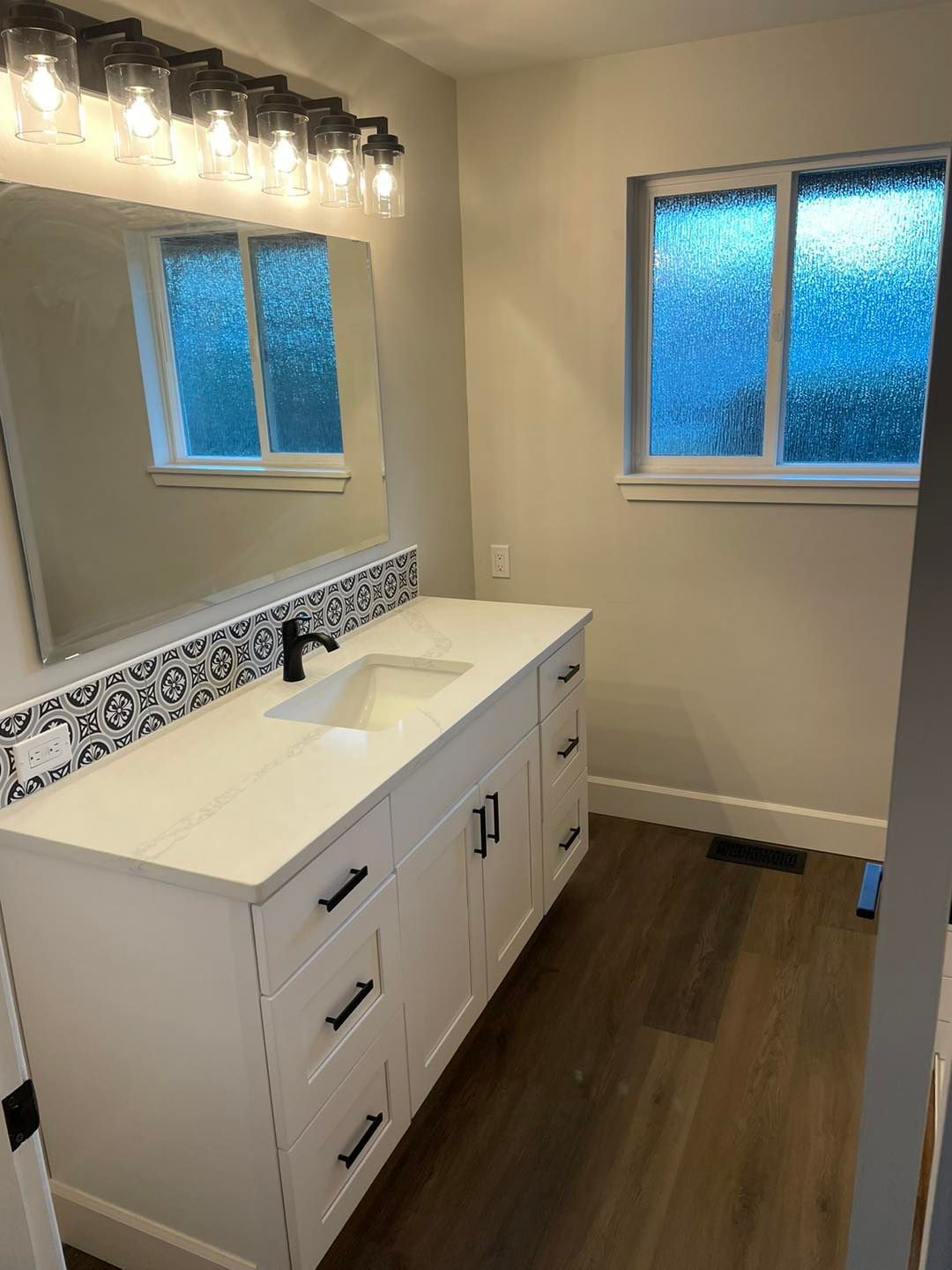 A bathroom with a sink , mirror and window.