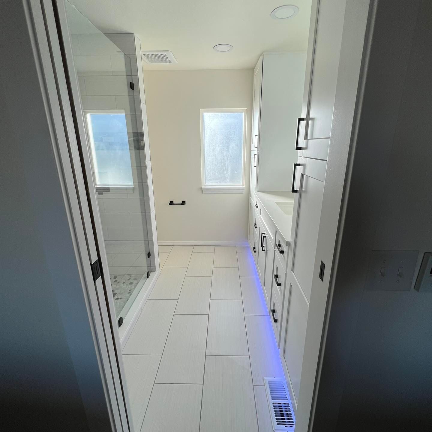A bathroom with white cabinets and a blue light on the floor.