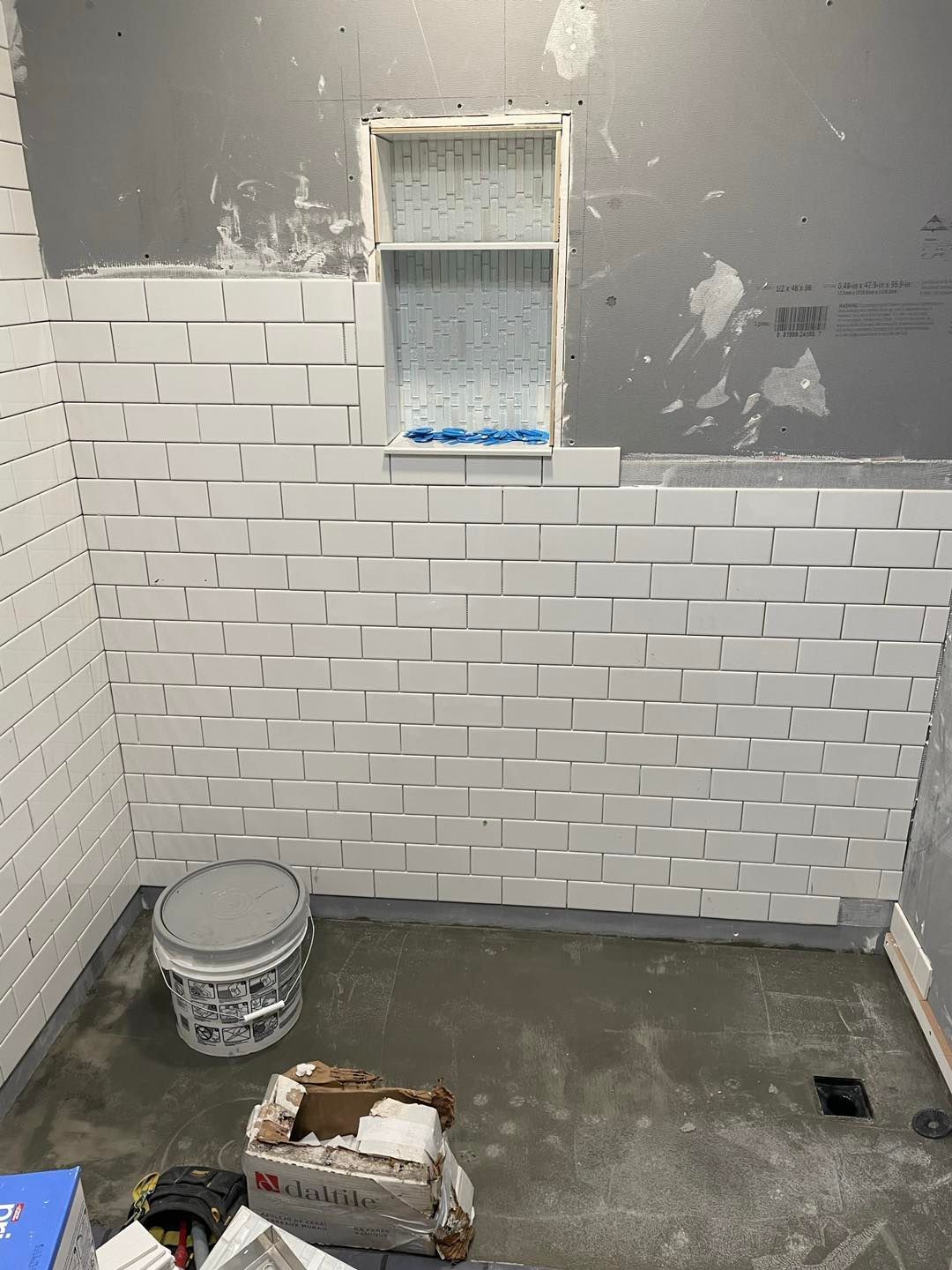 A bathroom with white brick walls and a bucket on the floor.