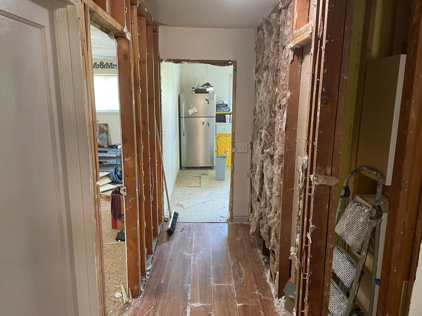 A hallway with a refrigerator and a ladder in it.