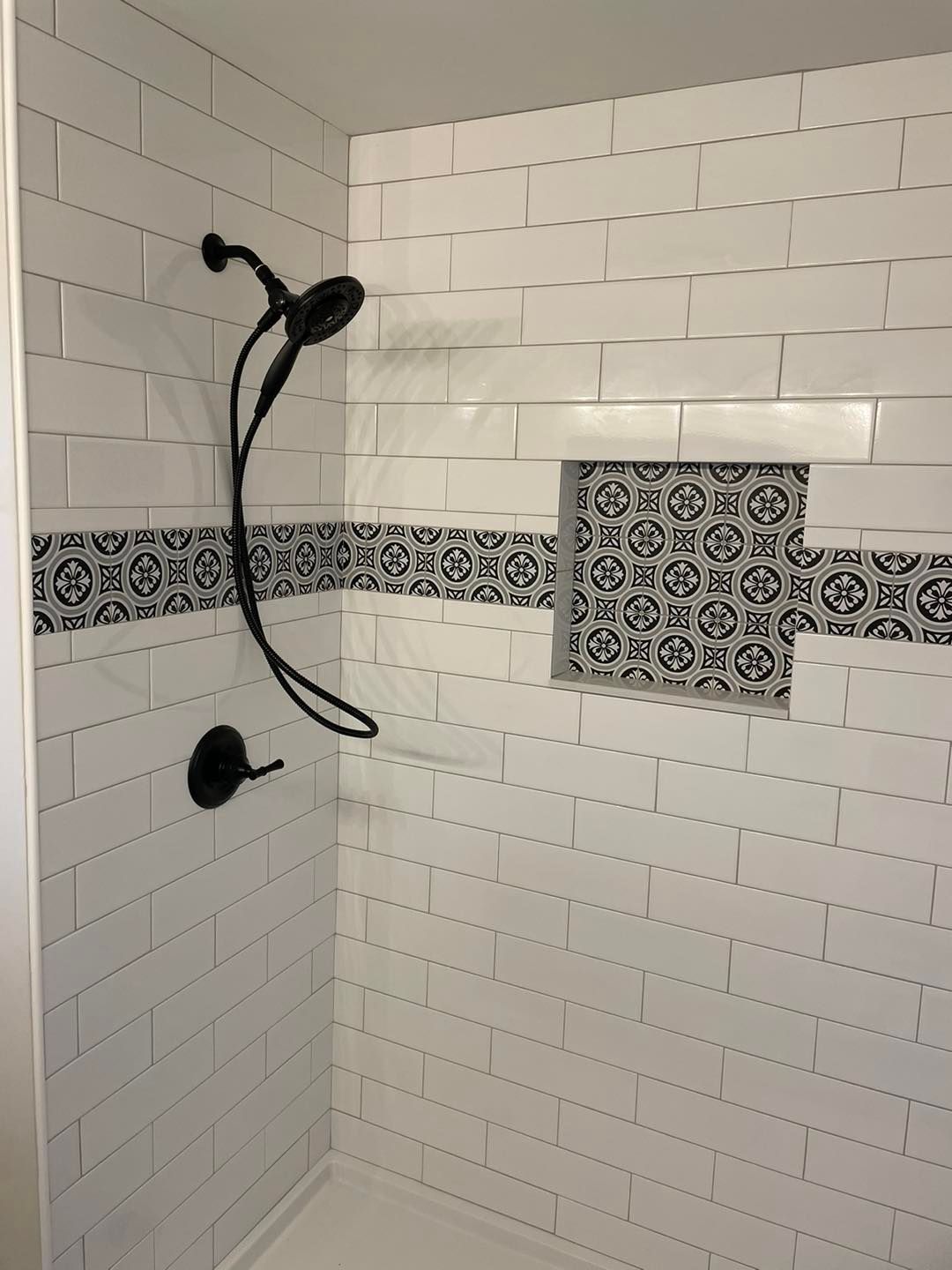 A shower with white tiles and a black shower head.