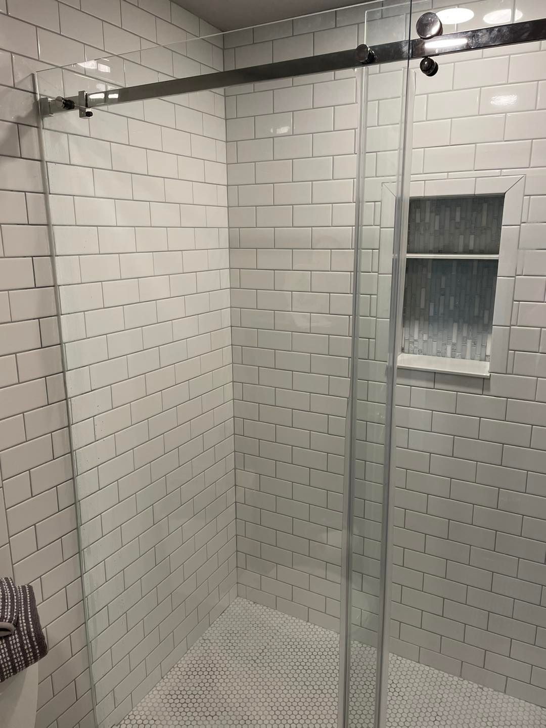 A bathroom with white tiles and a sliding glass shower door.
