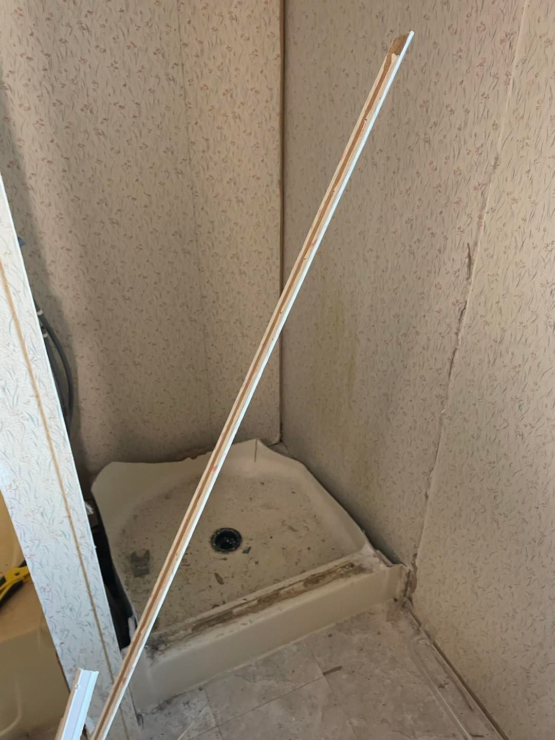 A bathroom with a shower stall and a wooden stick in the corner.