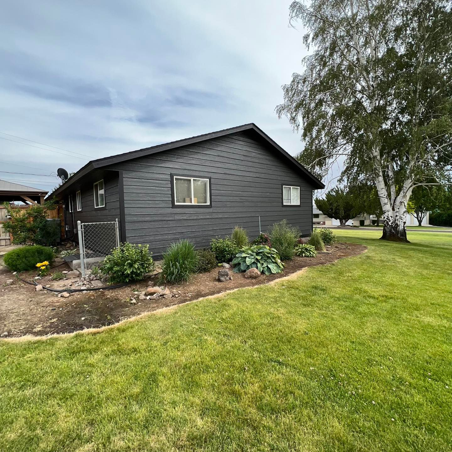 A black house with a lot of windows is sitting in the middle of a lush green field.