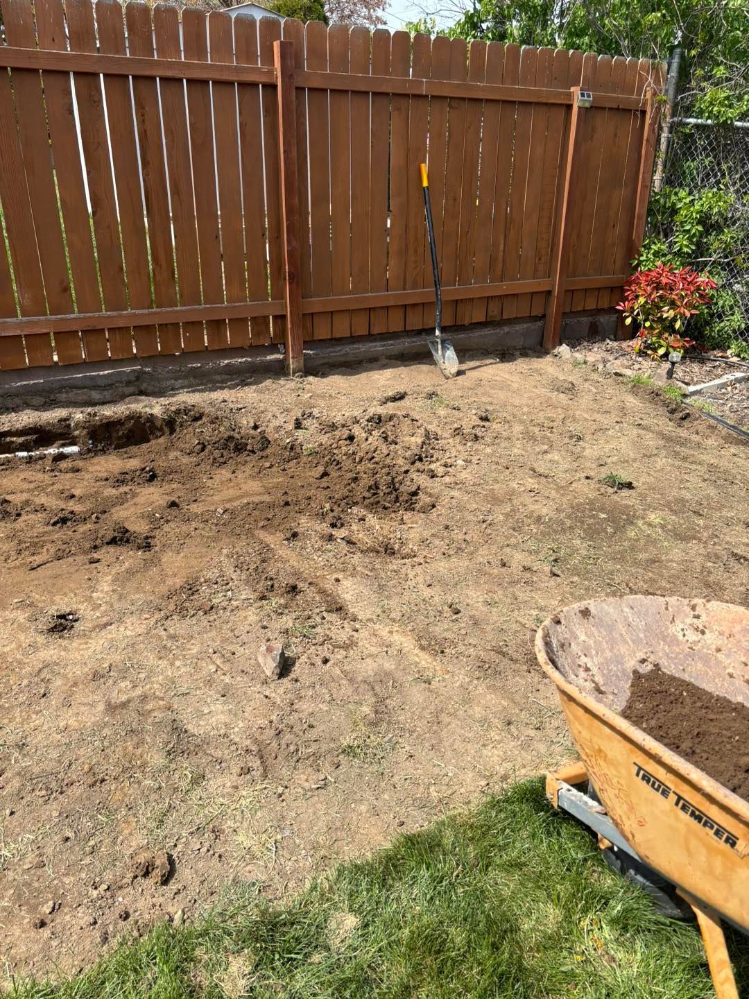 A wheelbarrow filled with dirt is sitting in front of a wooden fence.
