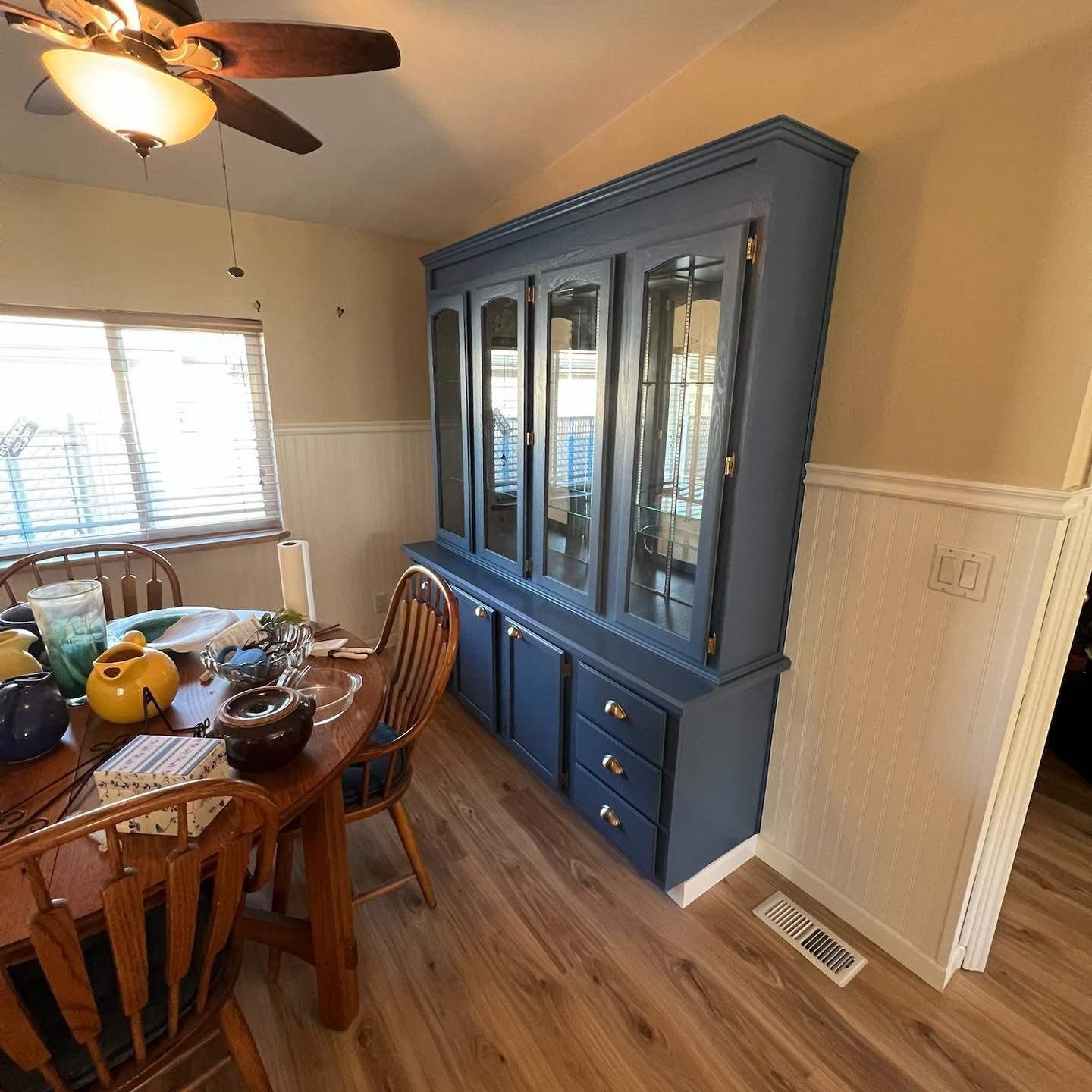 A dining room with a blue hutch and a ceiling fan