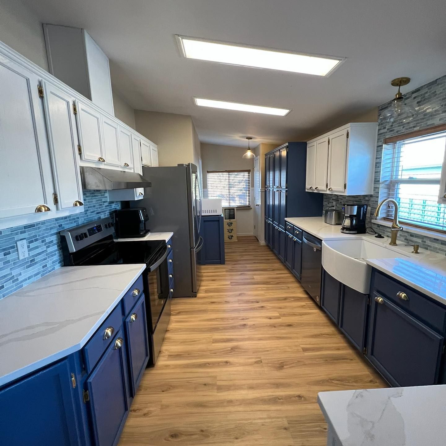 A kitchen with blue cabinets , a stove , a refrigerator , a sink , and a window.