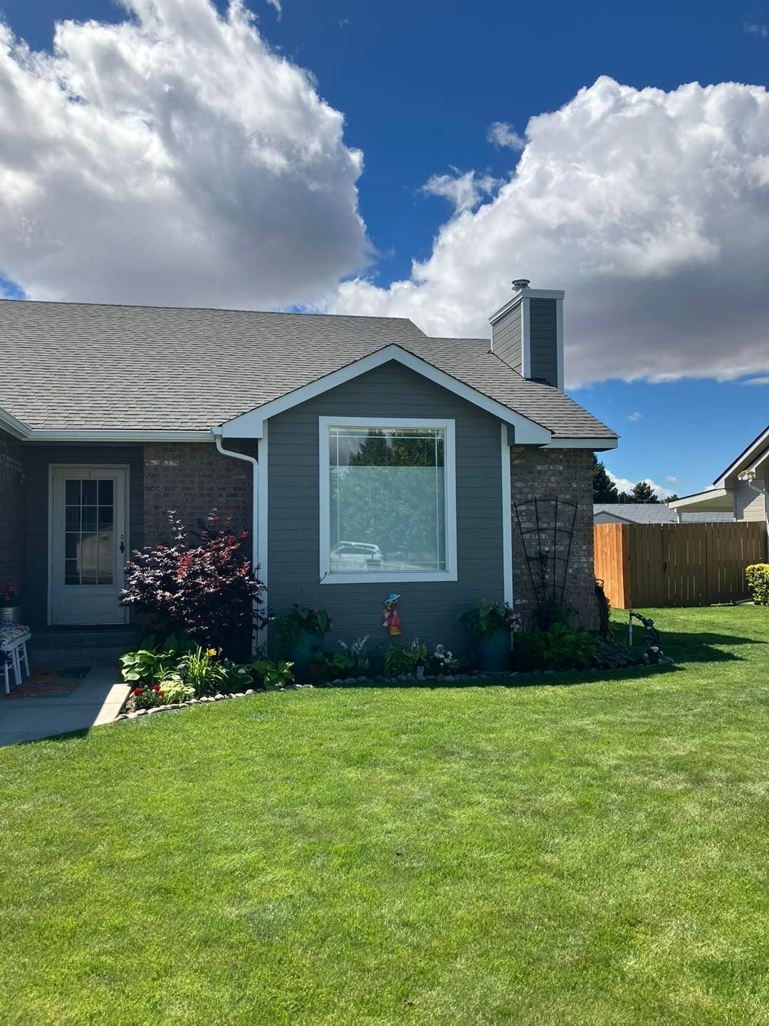 A house with a large window and a lush green lawn in front of it.