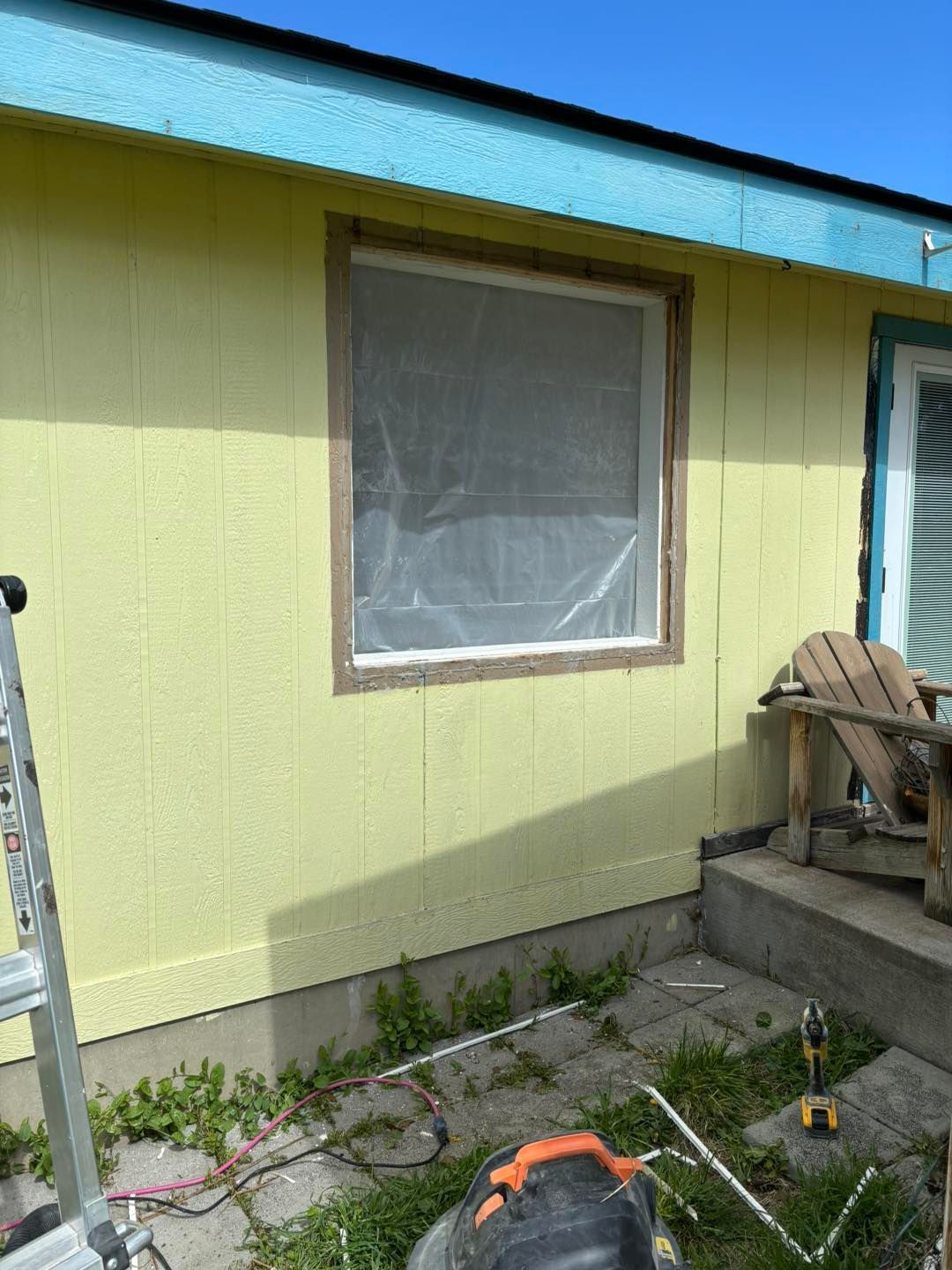 A yellow house with a window and a chair on the porch.