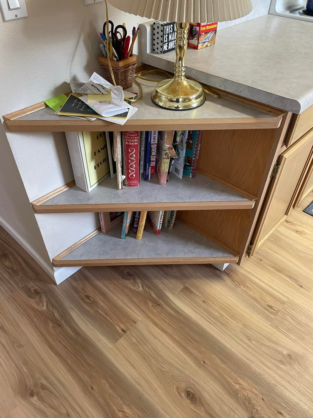 A corner shelf with books and a lamp on it in a kitchen.