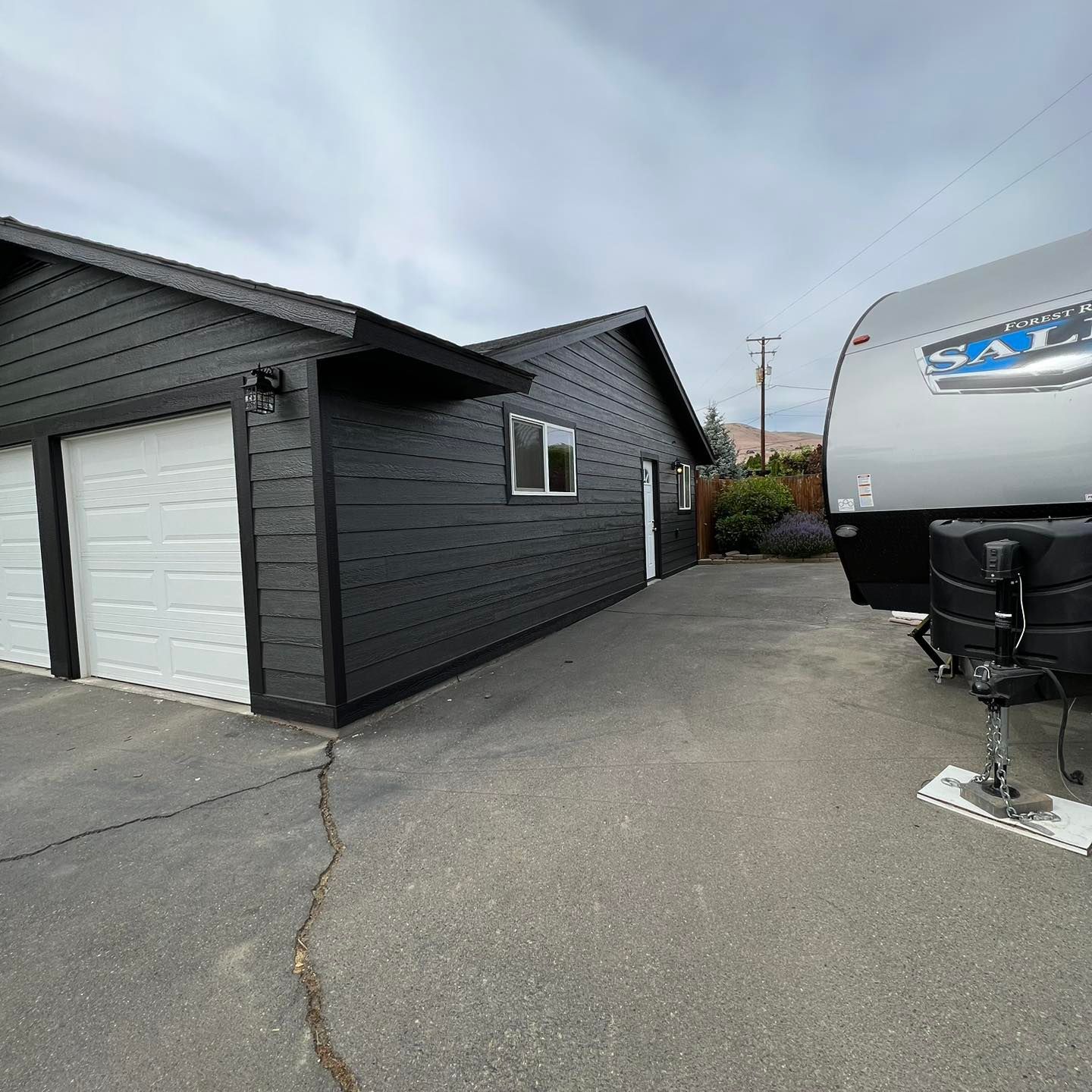A trailer is parked in front of a garage next to a house.