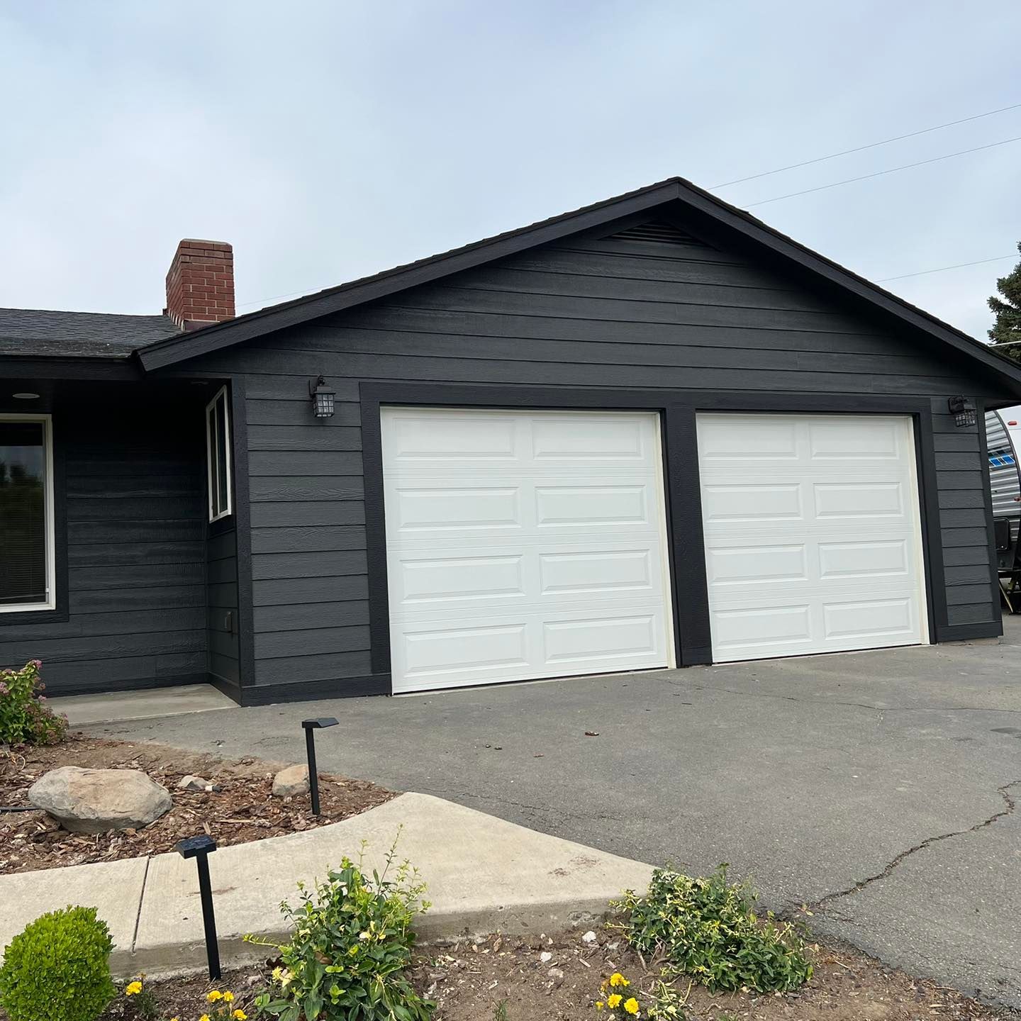 A black house with two white garage doors and a chimney.