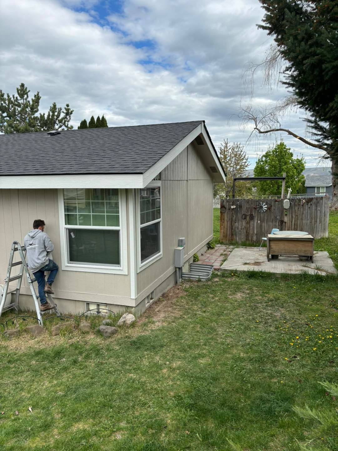 A man is sitting on a ladder painting the side of a house.