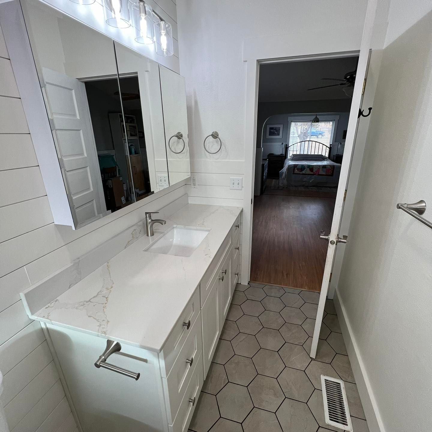 A bathroom with a sink , mirror , and hexagonal tile floor.