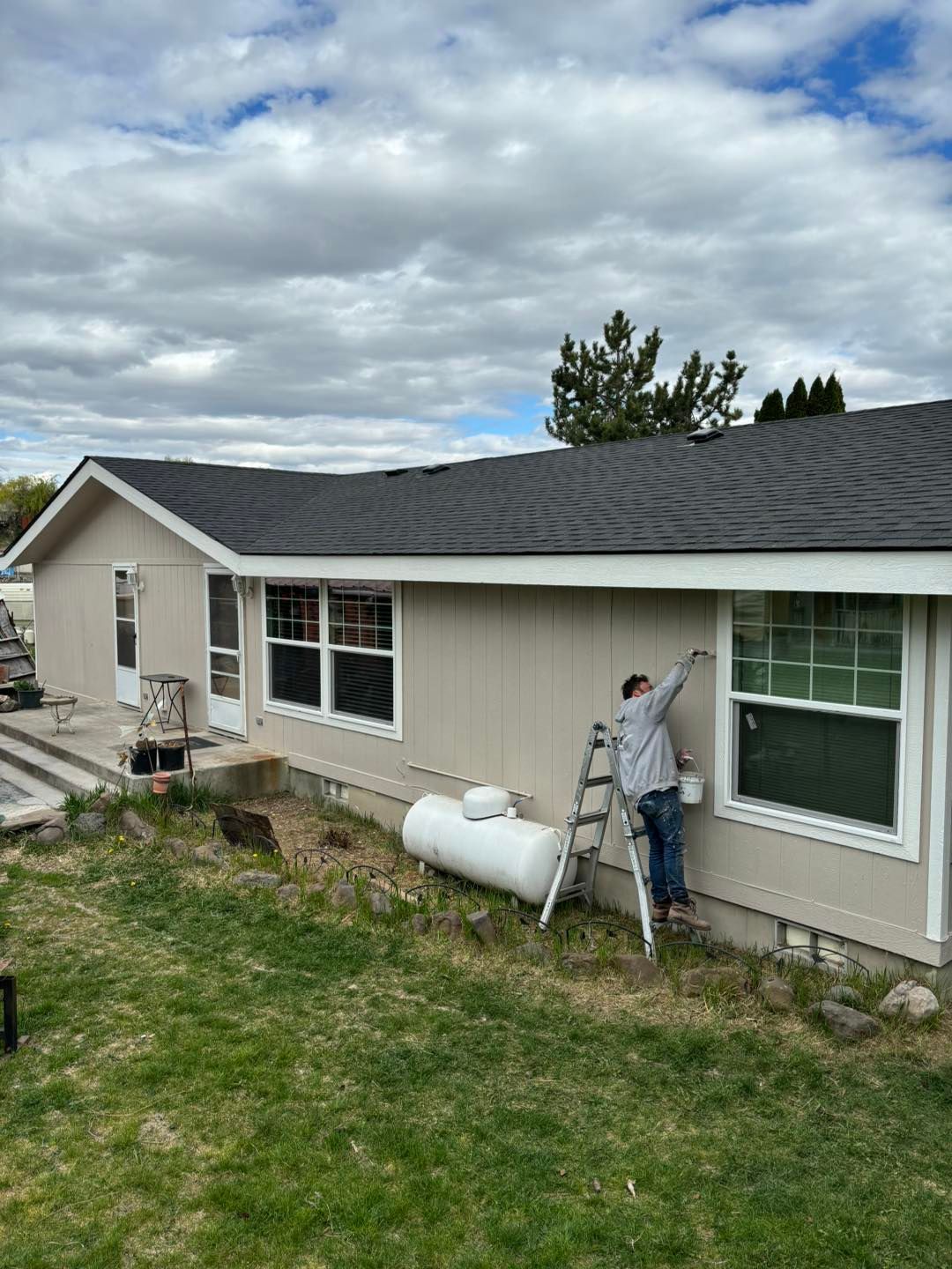 A man is standing on a ladder painting the side of a house.